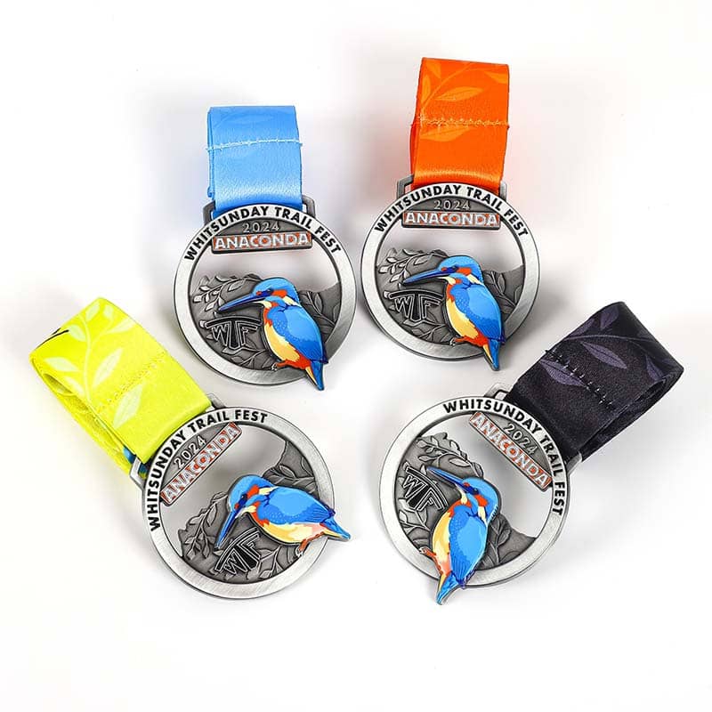 Four circular "Whitsunday Trail Fest 2024" medals, featuring a colorful kingfisher bird and vibrant ribbons in blue, orange, yellow, and black, showcase eye-catching custom merchandise on a white background.