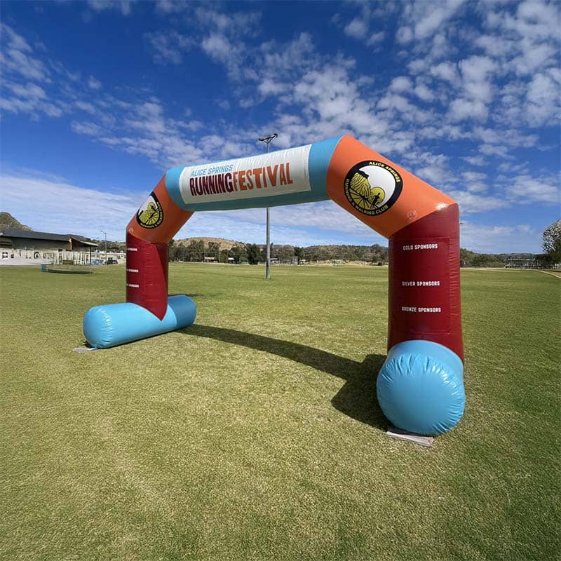 An inflatable arch labeled "Running Festival" stands on a grassy field under a partly cloudy sky, serving as custom merchandise and marking the start or finish line for the running event.